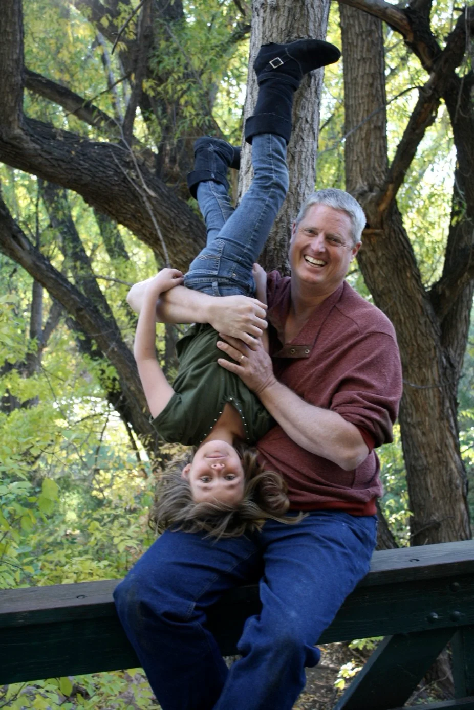 Man playfully holding a child upside down in a joyful outdoor setting.