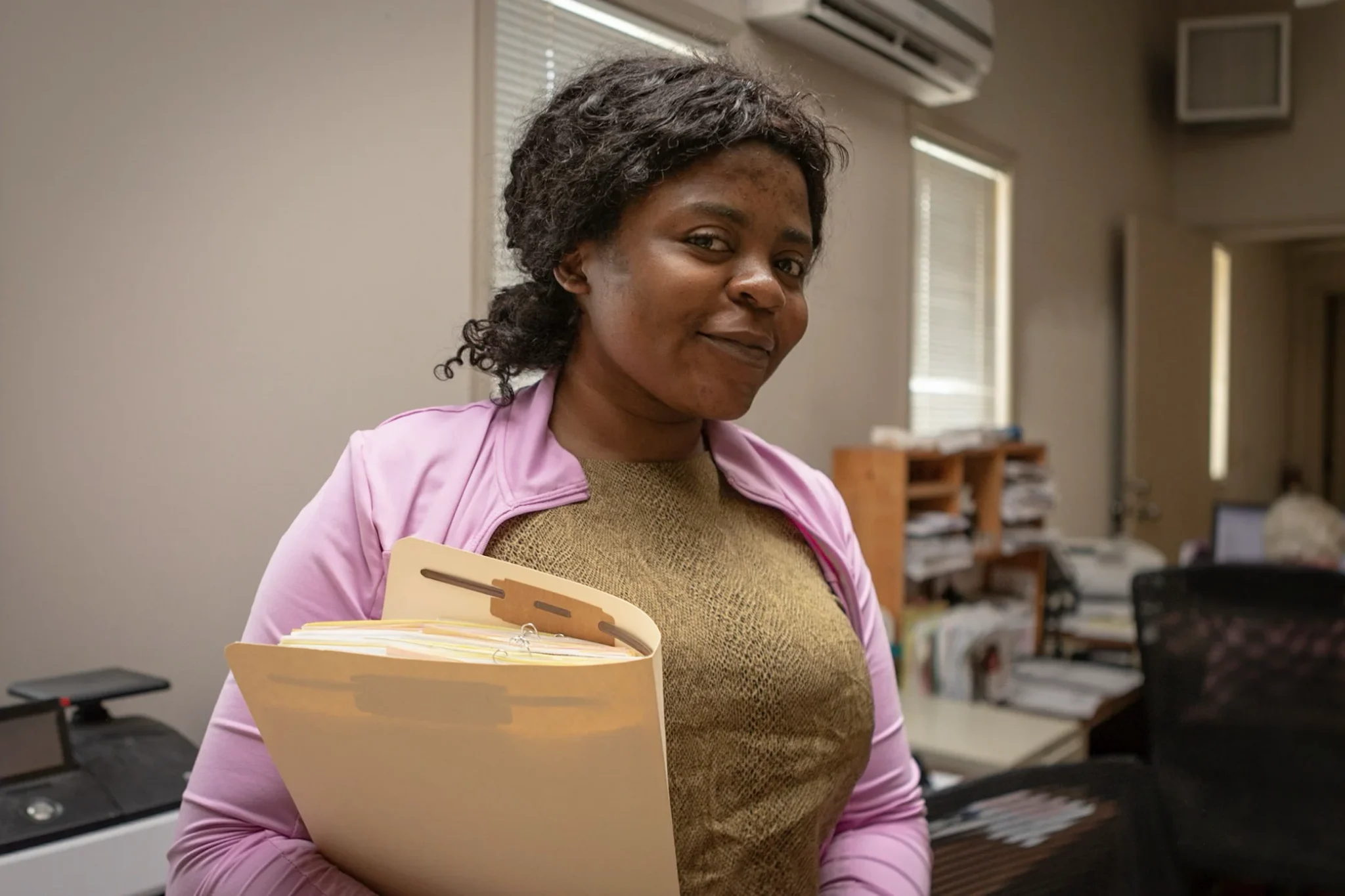 A woman holding files smiles in an office, representing support for foster families.