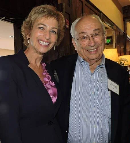 Two smiling individuals standing together indoors.