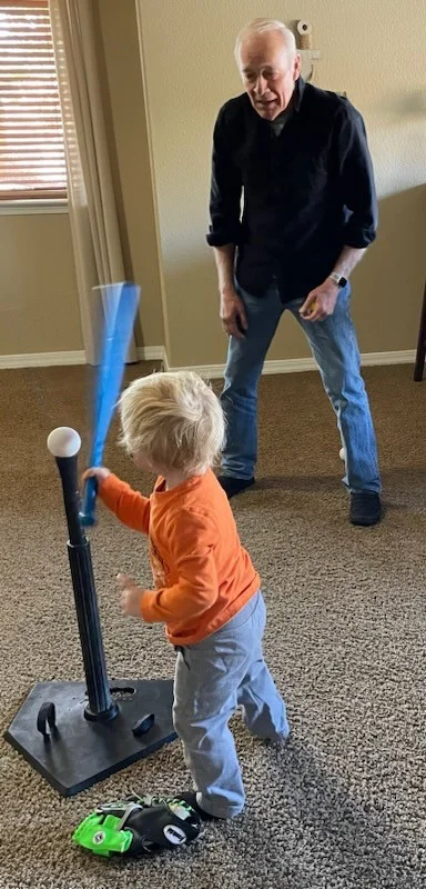 A foster grandparent supports a young child playing indoor baseball, highlighting the relational support in foster families.